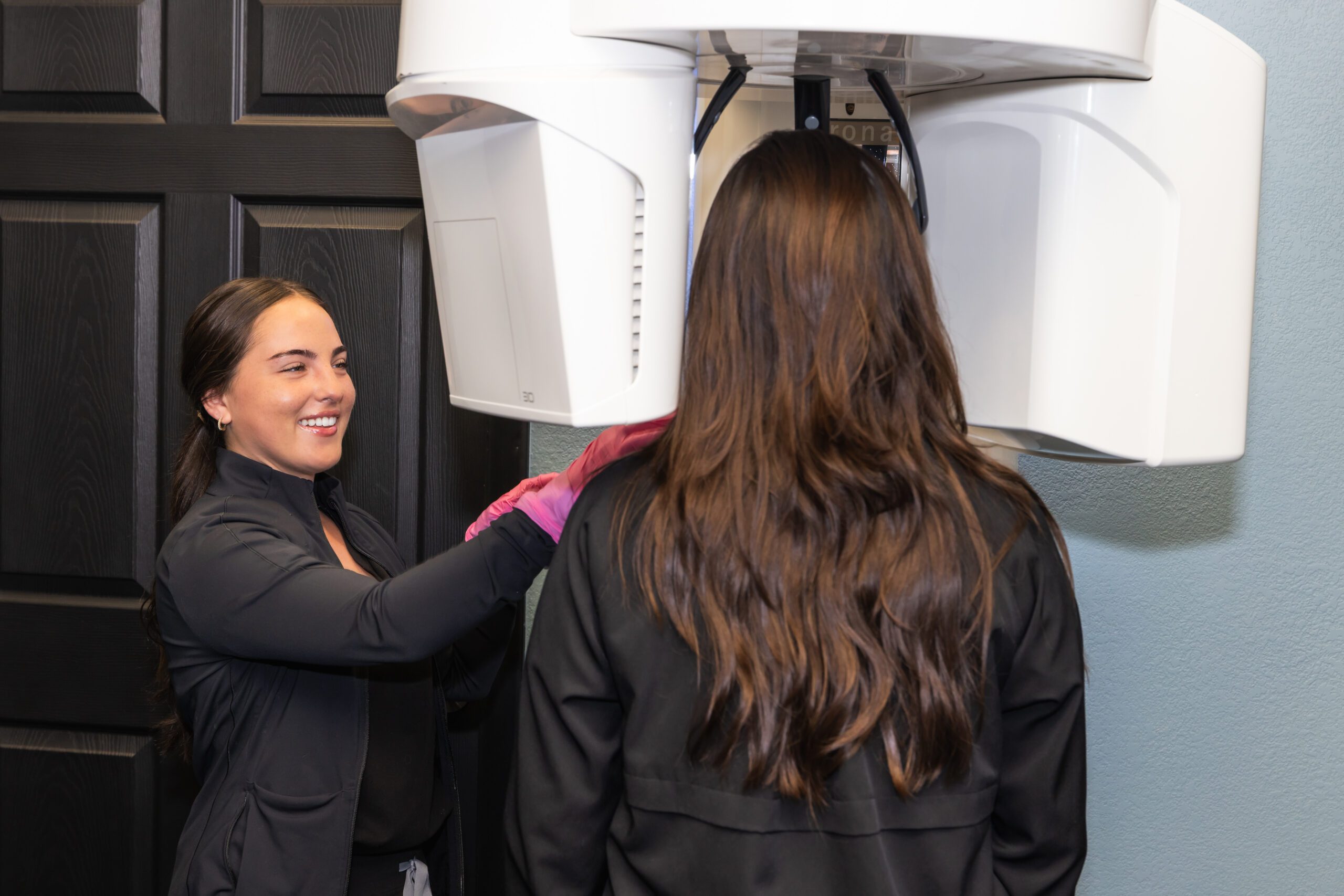 A dental staff smiles while preparing a patient for a panoramic X-ray